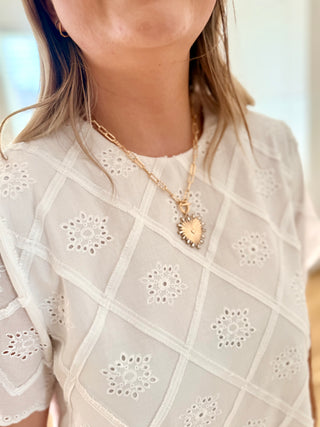 Person wearing a white blouse with lace details and a gold necklace with a heart pendant.