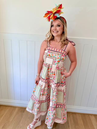 Woman wearing a colorful dress and headpiece against a white paneled wall.