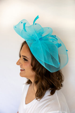 Woman wearing a turquoise fascinator hat against a white background
