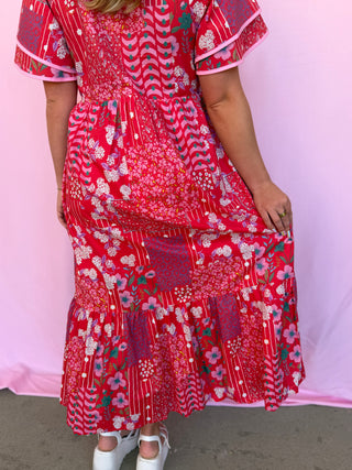Person wearing a red floral dress against a pink background