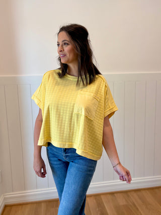 Woman wearing a yellow top and blue jeans against a white wall.