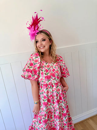 Woman wearing a pink floral dress and headpiece against a white wall.