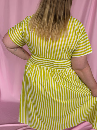 Person wearing a yellow and white striped dress against a pink background