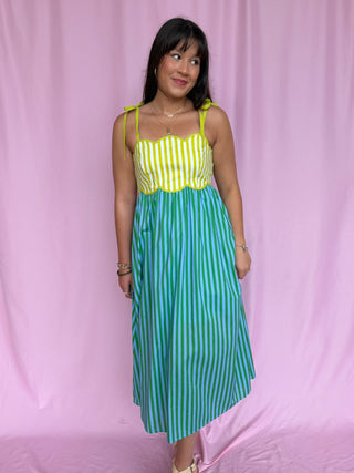 Woman wearing a yellow and green striped dress against a pink background