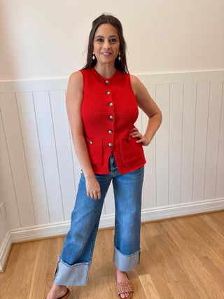 Woman wearing a red sleeveless top and blue jeans indoors.