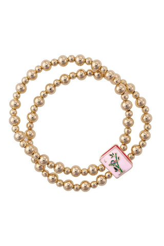 Gold beaded bracelet with a pink charm featuring a floral design on a white background