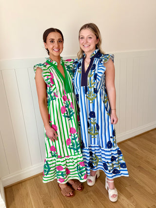 Two women wearing colorful dresses standing indoors against a white paneled wall.