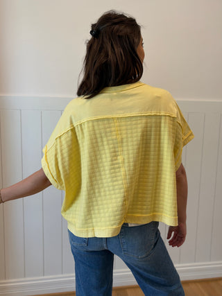 Person wearing a yellow sheer top and blue jeans against a white paneled wall.