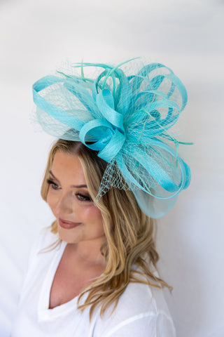 Woman wearing a turquoise fascinator hat against a white background