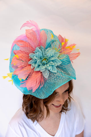 Woman wearing a colorful hat with pink and yellow feathers and a blue flower on a white background