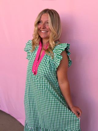 Woman wearing a green and white checkered dress with a pink shirt underneath against a pink background