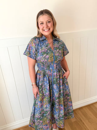 Woman wearing a floral dress standing against a white paneled wall.