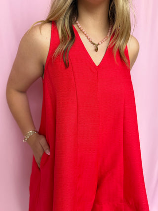 Person wearing a red sleeveless dress against a pink background