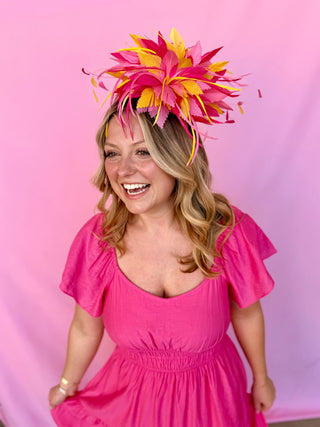 Woman wearing a bright pink dress and colorful headpiece against a pink background
