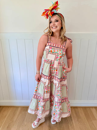 Woman wearing a colorful patterned dress and headband against a white paneled wall.