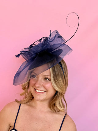 Woman wearing a navy blue decorative hat against a pink background
