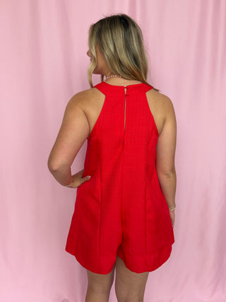 Woman wearing a red romper against a pink background