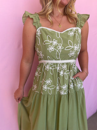 Green dress with white floral patterns worn by a person against a pink background