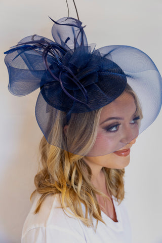 Woman wearing a navy blue fascinator with a veil on a plain background