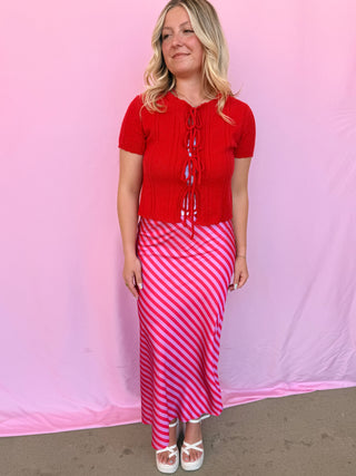 Woman wearing a red top and pink striped skirt against a pink background