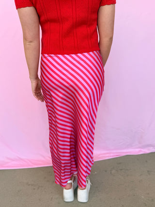 Person wearing a red sweater and pink and white striped skirt against a pink background