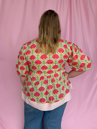 Person wearing a floral patterned blouse with a pink background