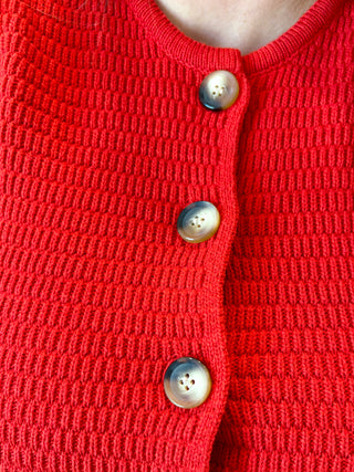 Close-up of a red knitted cardigan with pearl buttons.