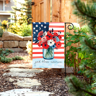 Decorative garden flag with American flag and floral design in a garden setting.
