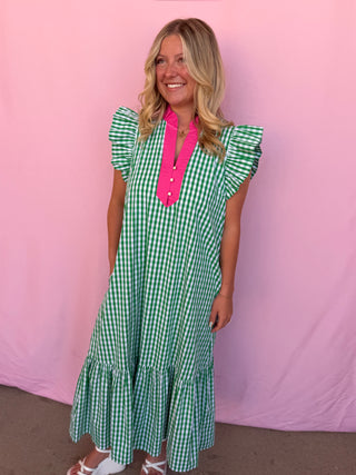 Woman wearing a green checkered dress with a pink shirt underneath against a pink background