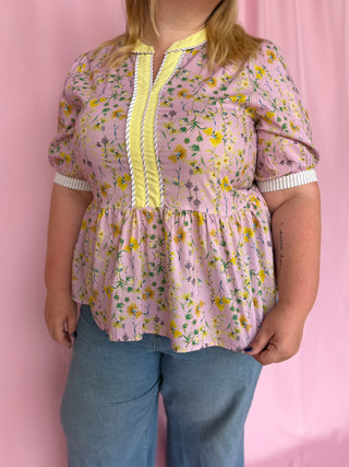 Person wearing a floral blouse with a yellow zipper against a pink background