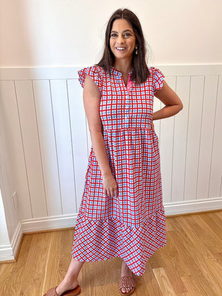 Woman wearing a red and white checkered dress standing in a room with wooden flooring and white walls.