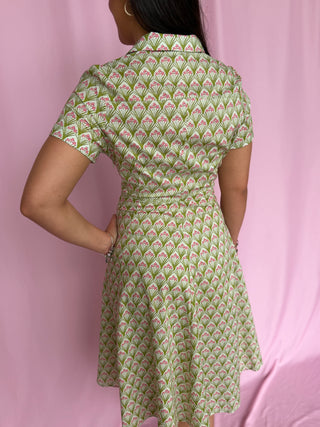 Person wearing a green patterned dress against a pink background