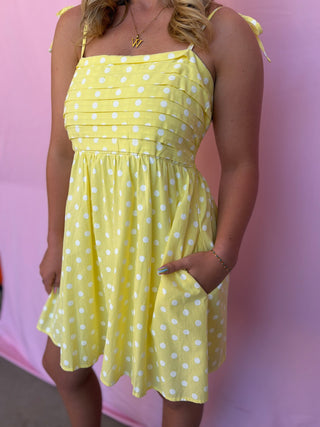 Woman wearing a yellow polka dot dress against a pink background