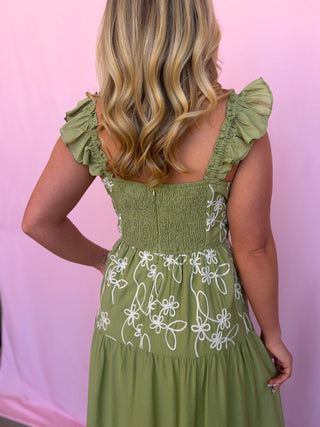 Woman wearing a green dress with floral embroidery against a pink background