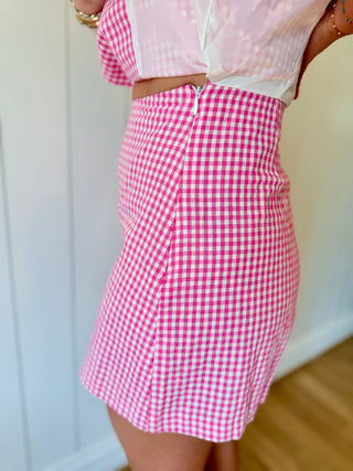 Person wearing a pink and white checkered skirt with a light pink top against a neutral background