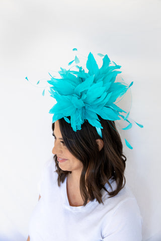 Woman wearing a turquoise feathered headpiece against a white background