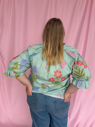 Person wearing a floral blouse with puffed sleeves against a pink background