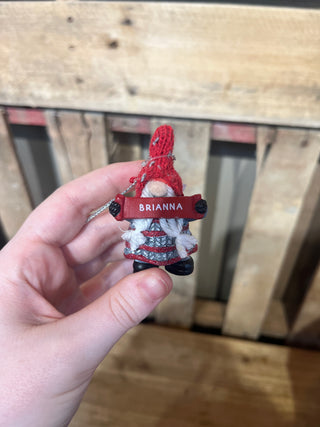 Hand holding a small red and white decorative item with 'Briannna' on it against a wooden background.