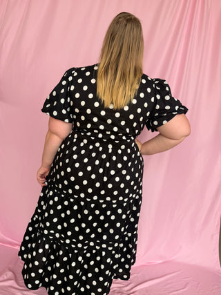 Person wearing a black polka dot dress against a pink background