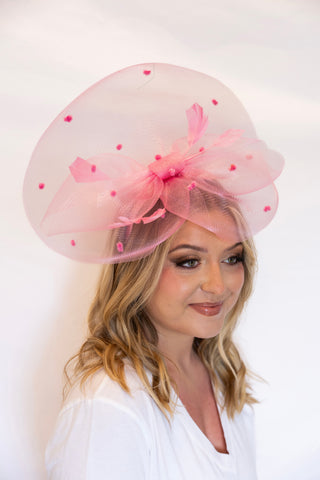 Woman wearing a large pink hat with polka dots and a bow against a white background