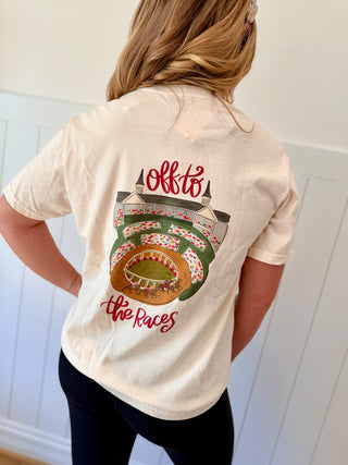 Person wearing a cream t-shirt with a graphic design and text on the back, standing against a white wall.