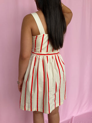 Person wearing a white dress with red stripes against a pink background