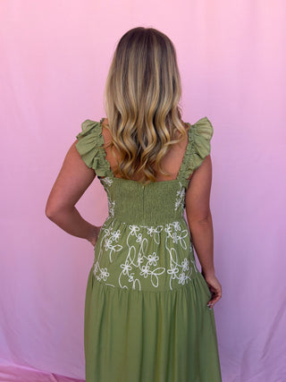 Woman wearing a green dress with floral embroidery against a pink background