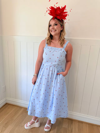 Woman wearing a blue dress with a red floral headpiece against a white paneled wall.