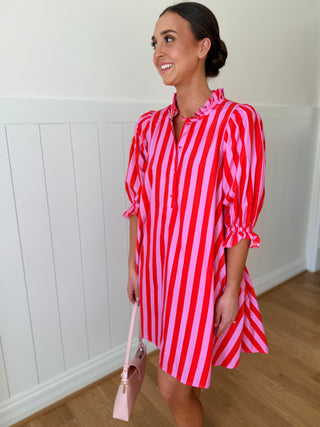 Woman wearing a red and pink striped dress holding a pink handbag indoors.