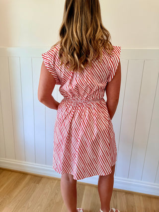 Person wearing a red and white striped dress against a white paneled wall.