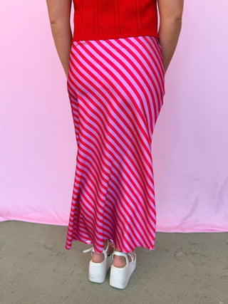 Person wearing a red top and pink and white striped skirt on a pink background
