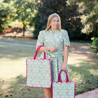 Woman in a green patterned dress holding two matching bags outdoors.