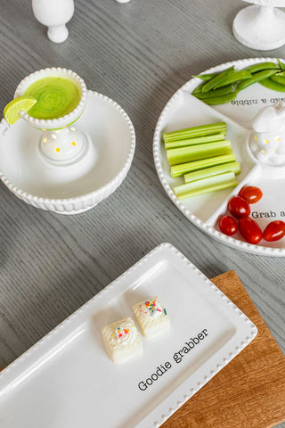 Assorted snacks on a white plate with 'Goodie Grabber' branding on a wooden surface.