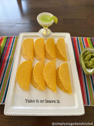 Tortilla chips on a platter with a small bowl of guacamole on a colorful placemat.